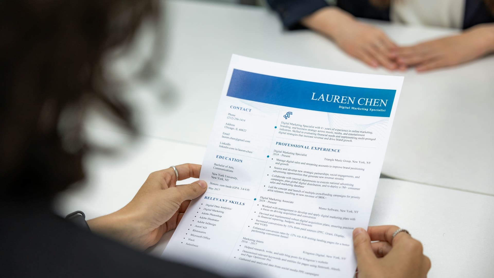 Personne lisant un CV imprimé pendant un entretien, face à une autre personne assise de l'autre côté de la table