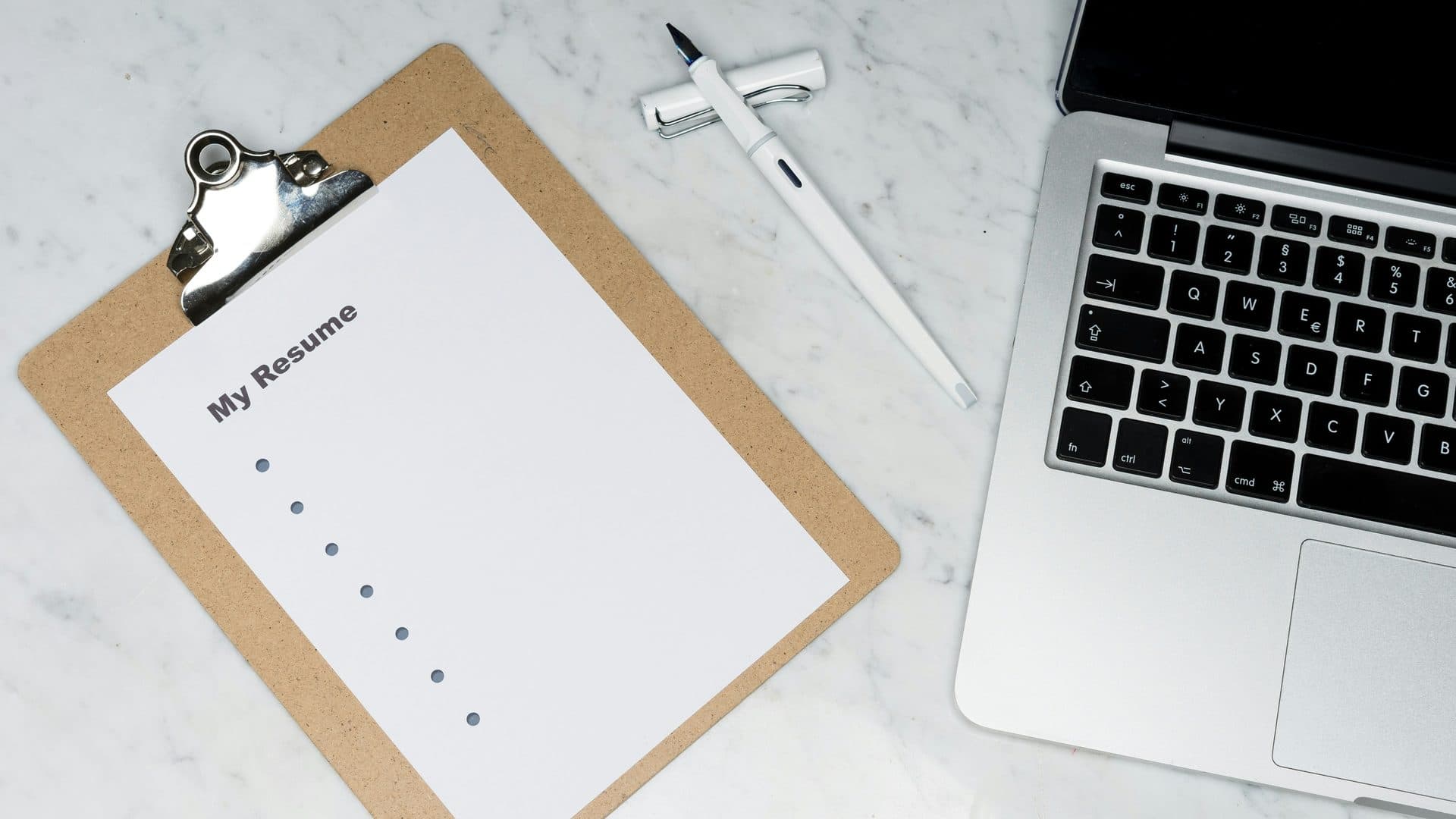 Un CV vierge sur un porte-documents, à côté d'un stylo plume et d'un ordinateur portable